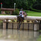 Horse and rider jumping over a log obstacle in an equestrian XC competition.