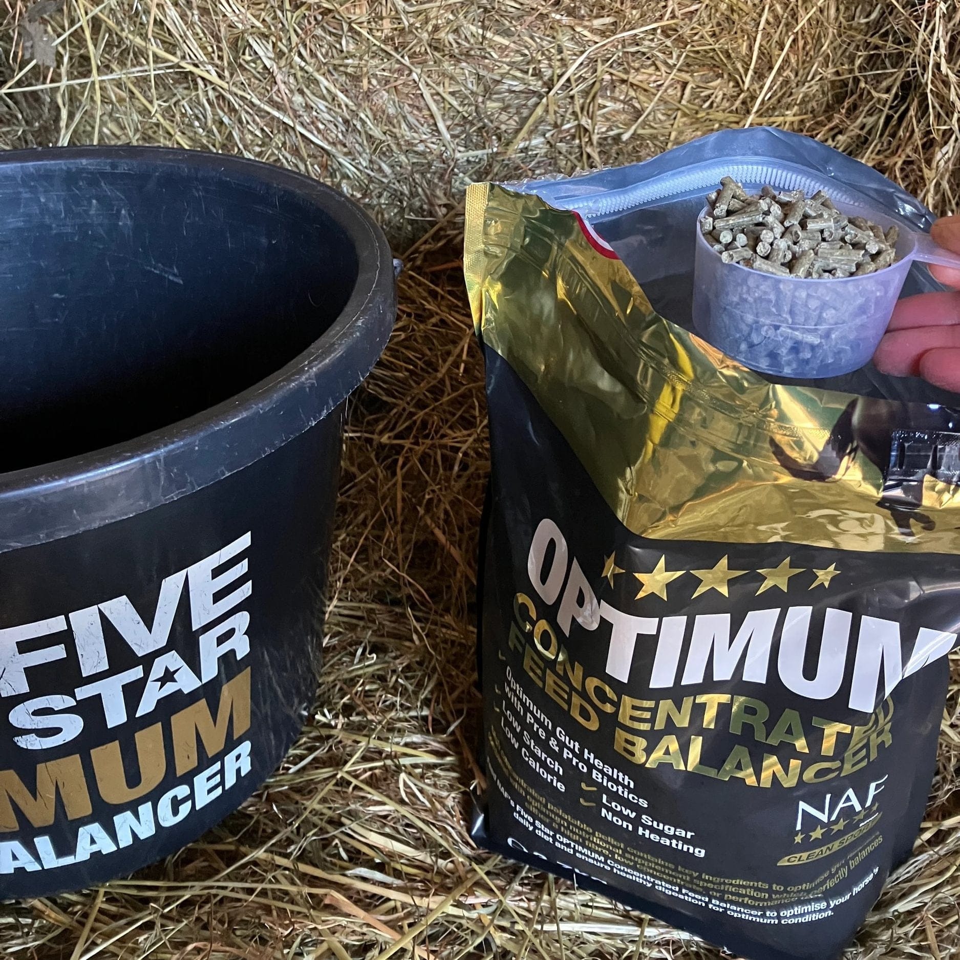 Bag of NAF Optimum Concentrate Feed Balancer on hay with a black container labeled 'Five Star Mum'.